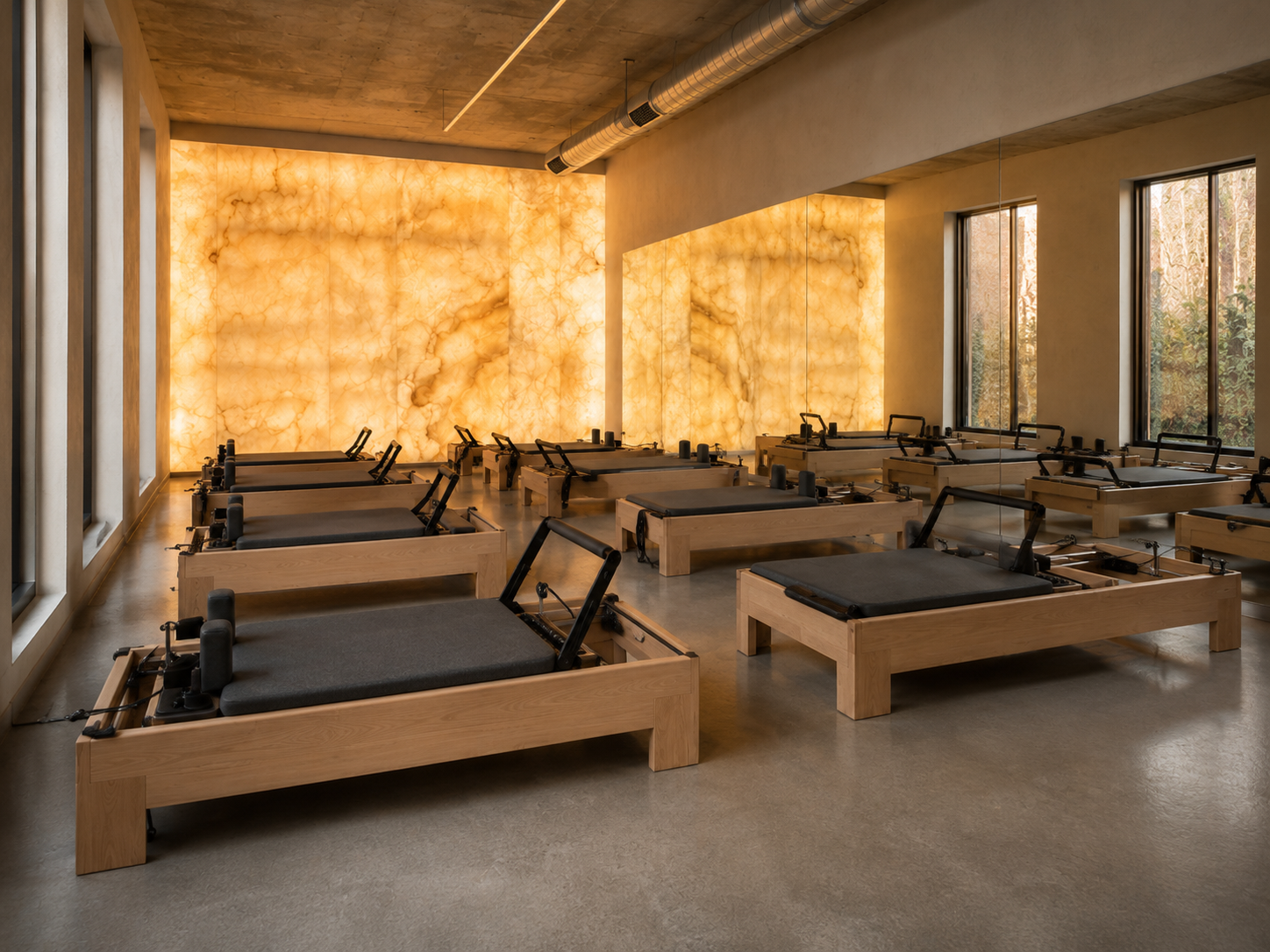 Wide view of STRIA's private Pilates studio with rows of wood reformers facing a glowing onyx wall